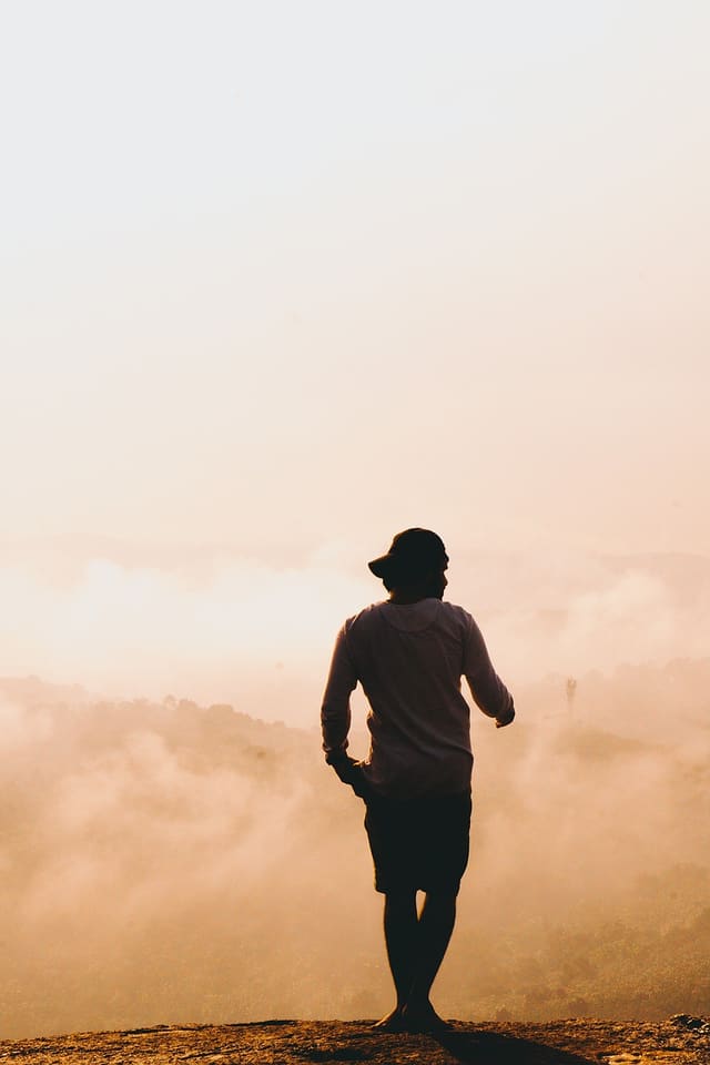 A lone figure standing on a ridge above a valley filled with morning fog.