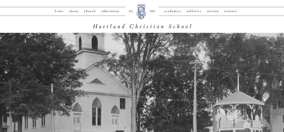 The Hartland Christian School home page on a desktop screen: a crest, a serif wordmark and a black-and-white photograph of the village church.